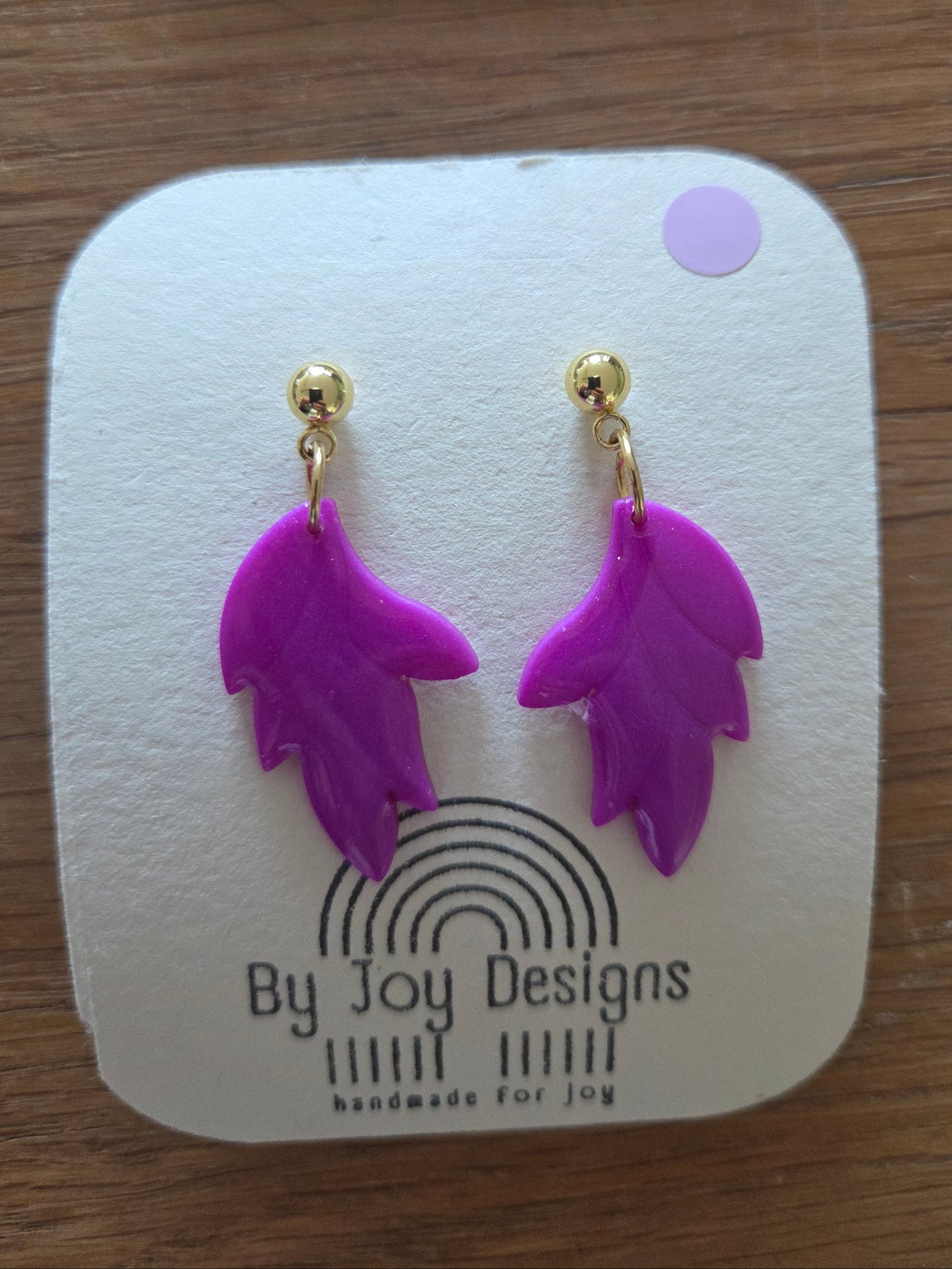Fuchsia bladvormige oorhangers van polymeerklei aan gouden bolletjesstuds, op een wit By Joy Designs kaartje