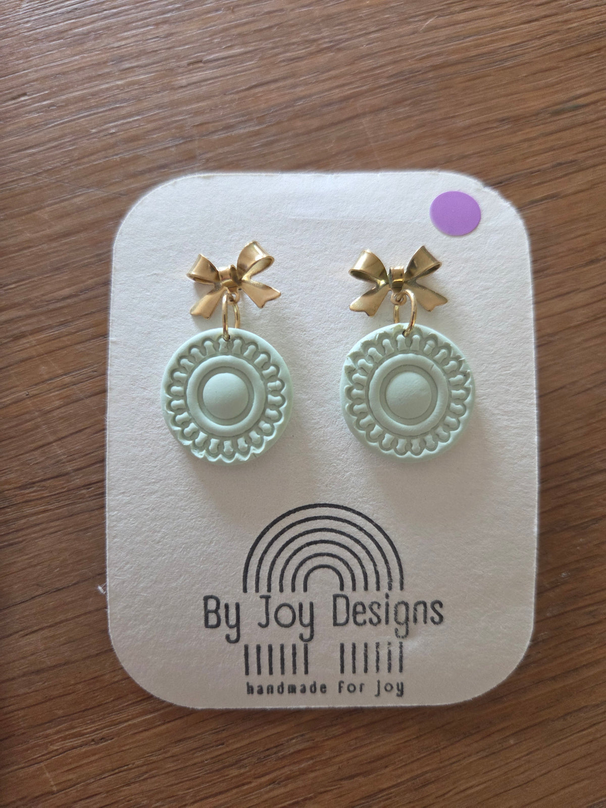 Mintkleurige ronde hangers met kantachtig reliëf aan gouden strik-oorstekers op een wit By Joy Designs kaartje
