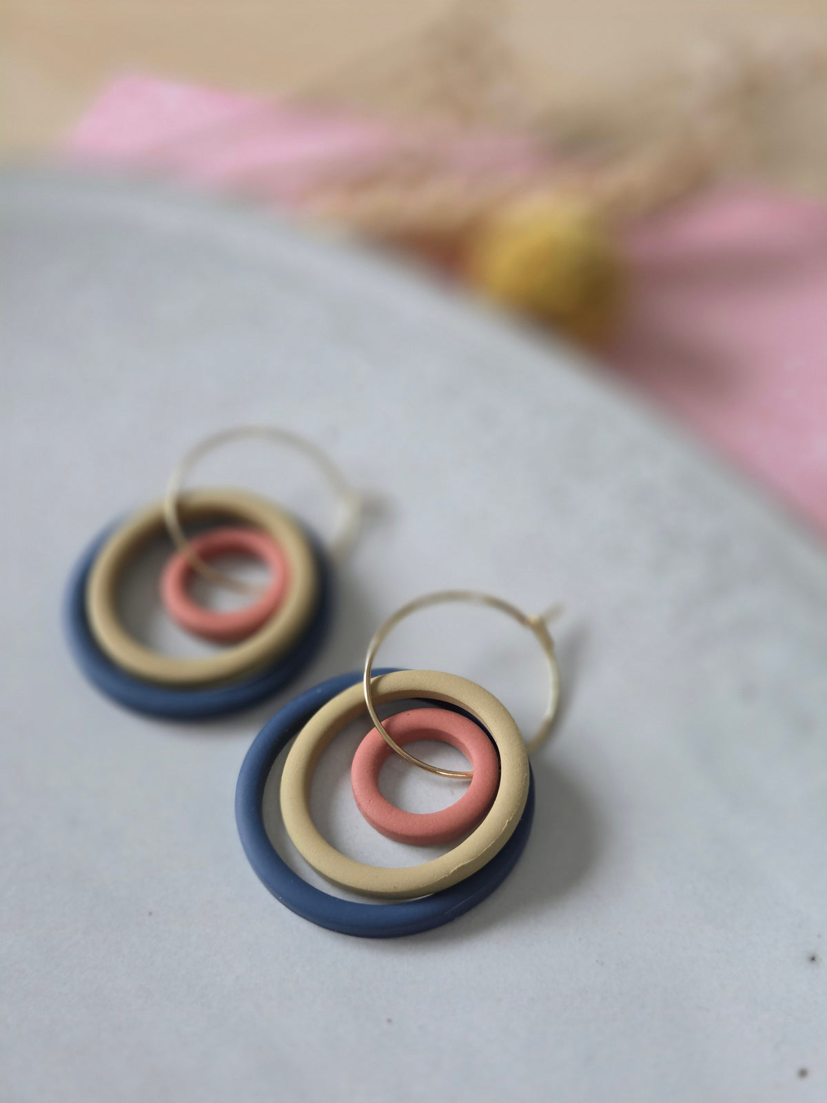Drie ringen in verschillende groottes van diep blauw, terracotta en mosterd geel oorbellen aan een gouden hoop.