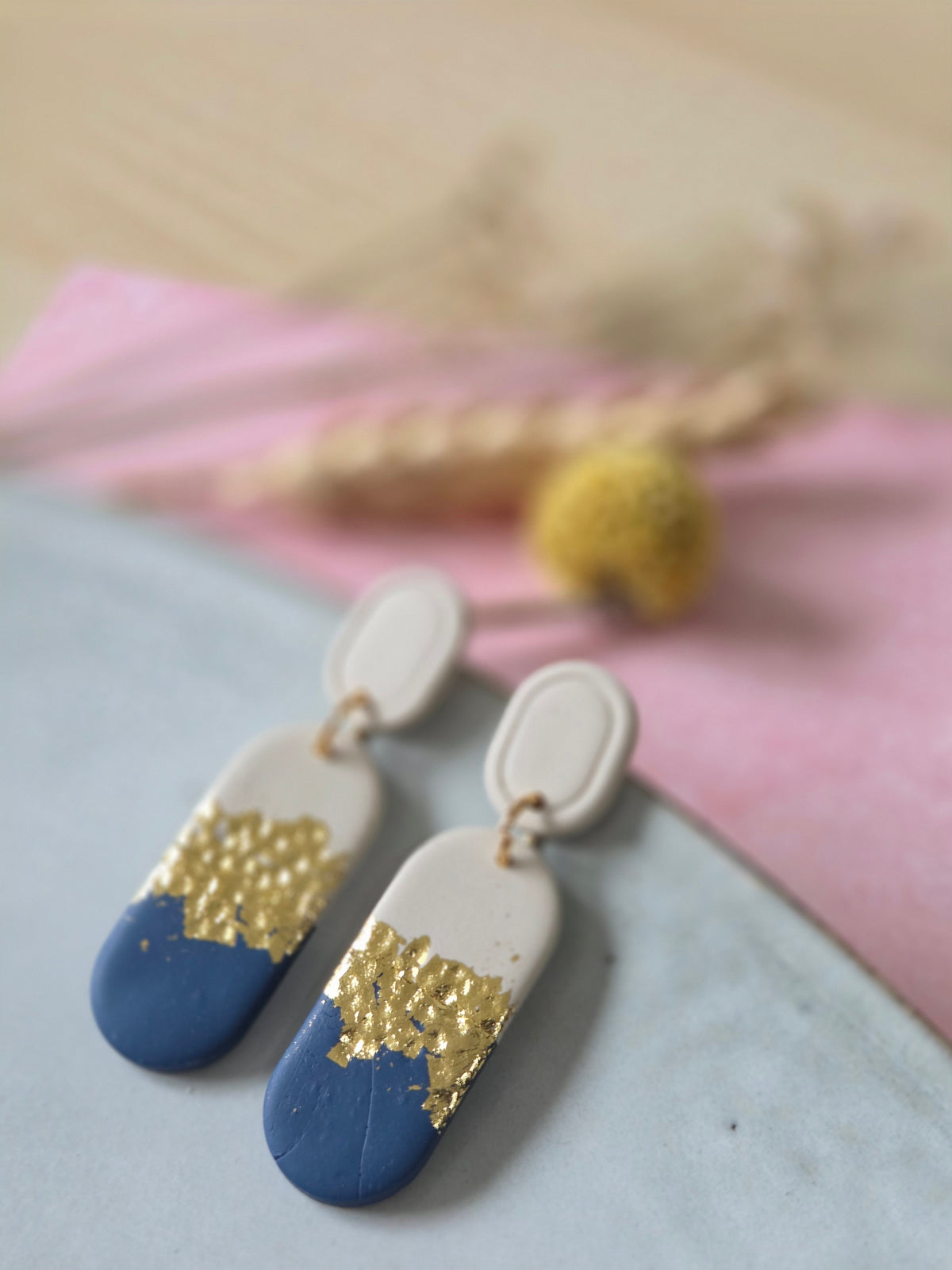 Ovalen oorbellen met donkerblauw en beige met een bladgoud band aan beige ovalen oorstekers.