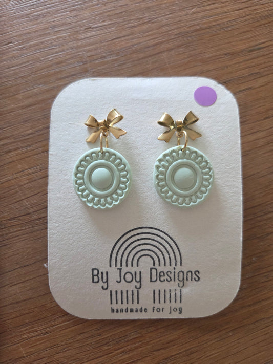 Mintkleurige ronde hangers met kantachtig reliëf aan gouden strik-oorstekers op een wit By Joy Designs kaartje