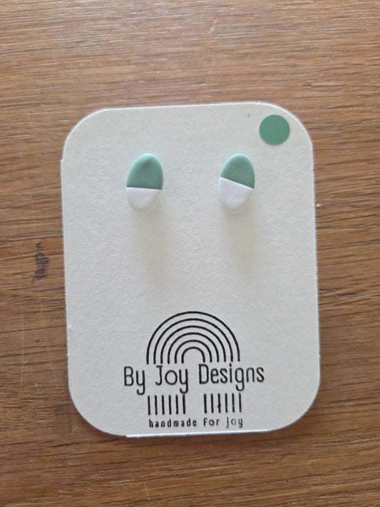 Kleine ovale studs van polymeerklei, half saliegroen en half wit, op een wit By Joy Designs kaartje
