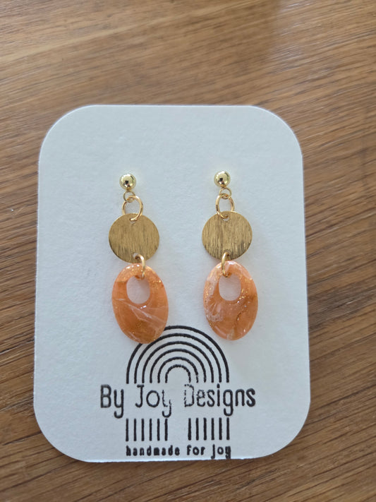 Ovale ambergemarmerde hangers met goudflakes en open venster aan geborstelde gouden rondjes op een By Joy Designs kaartje