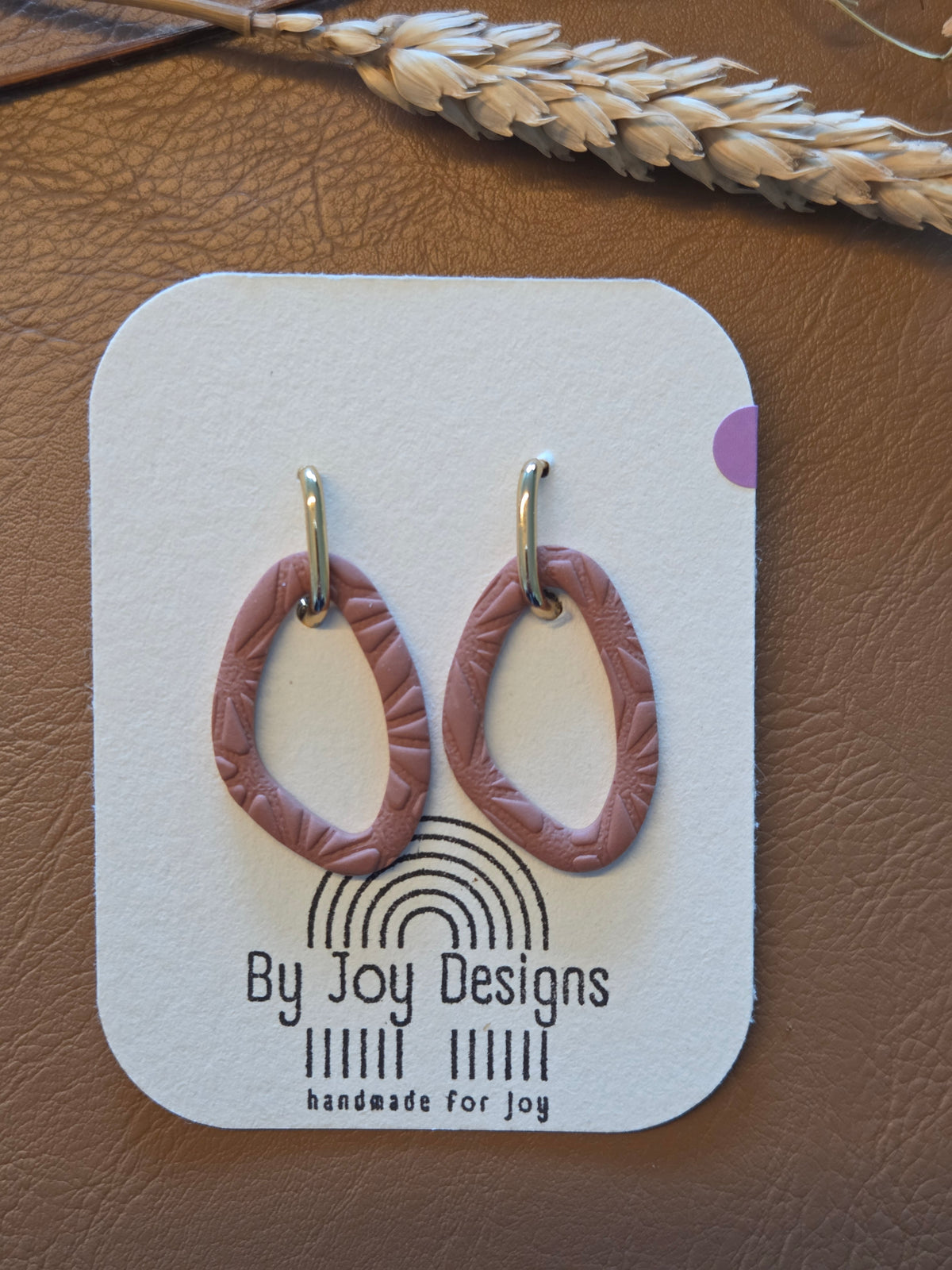 Mauve organische open hangers van polymeerklei met bloemenreliëf aan gouden U-vormige studs op een By Joy Designs kaartje