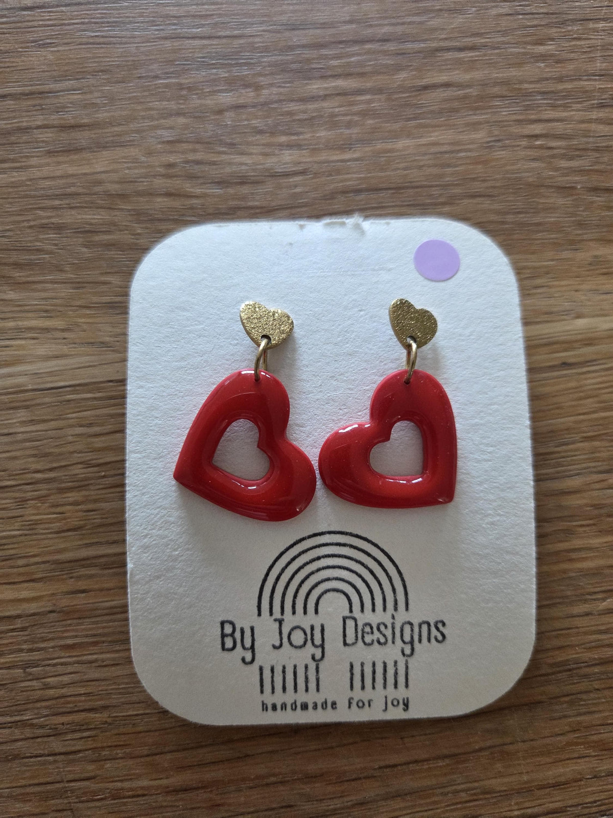 rode open hartjes van polymeerklei met glanzende resin aan gouden hartvormige oorstekers, op een wit By Joy Designs kaartje